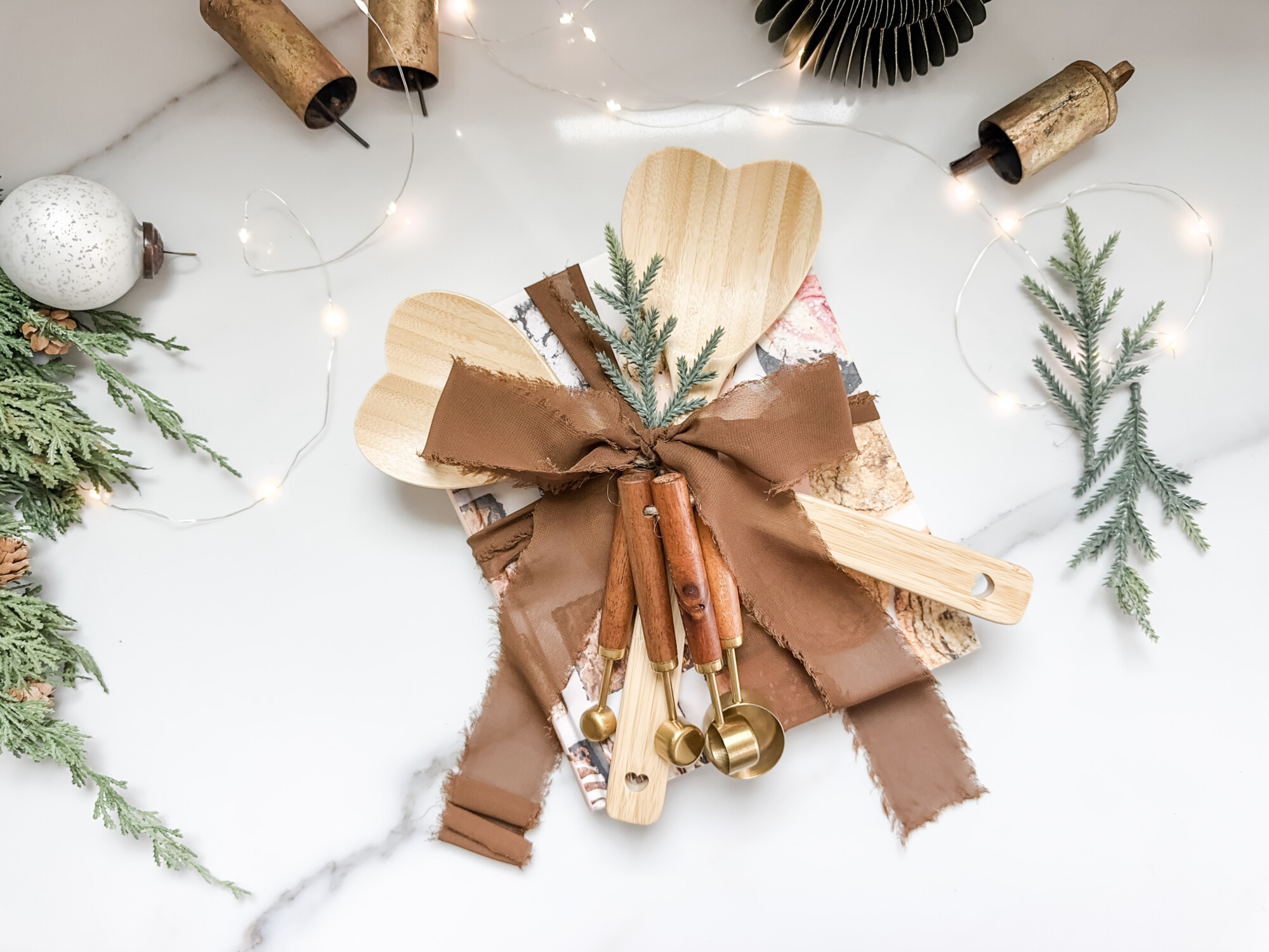thoughtful and affordable diy host gifts under $35 | host gifts, diy gifts, gift ideas, handmade gift, gift ideas, cooking, baking gift, brown fringe ribbon, measuring spoon, heart spoons, bells, pine stems 