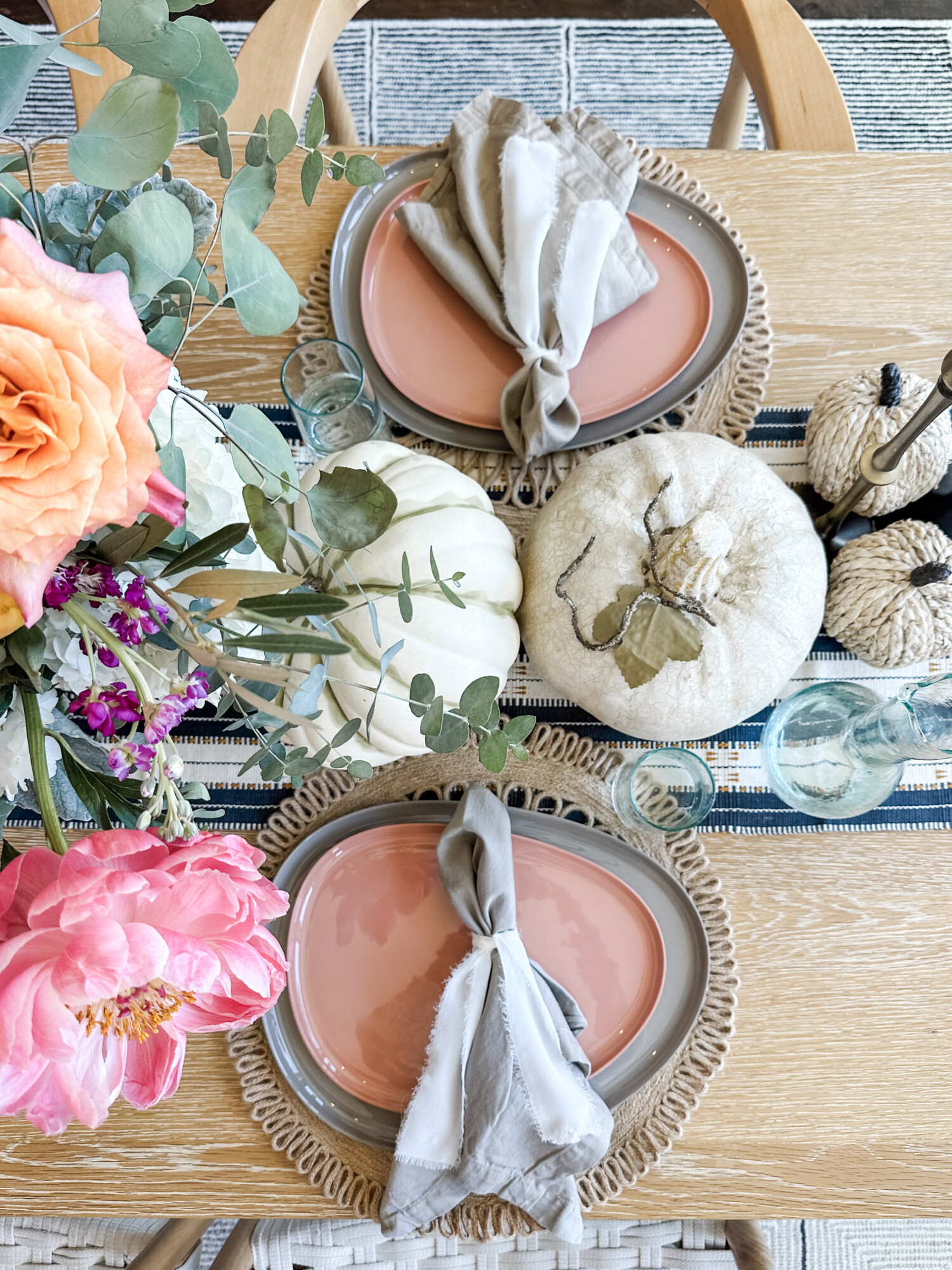 Warm fall table décor featuring peach plates, linen napkins, and neutral pumpkins accented with bright floral arrangements and eucalyptus, perfect for a modern Thanksgiving tablescape.