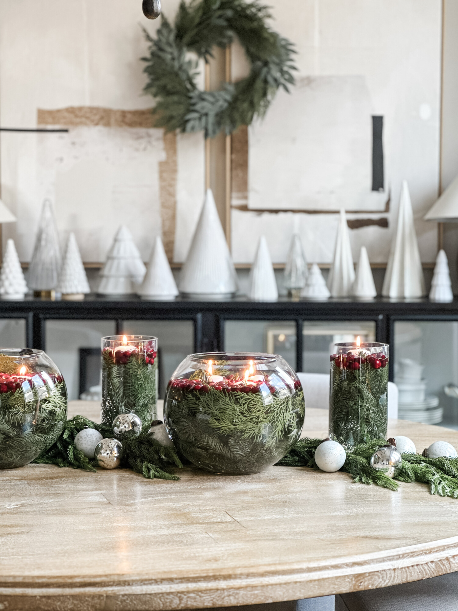 Creative Christmas centerpiece idea using clear glass vases filled with greenery, cranberries, and floating candles for a simple and elegant holiday table display.