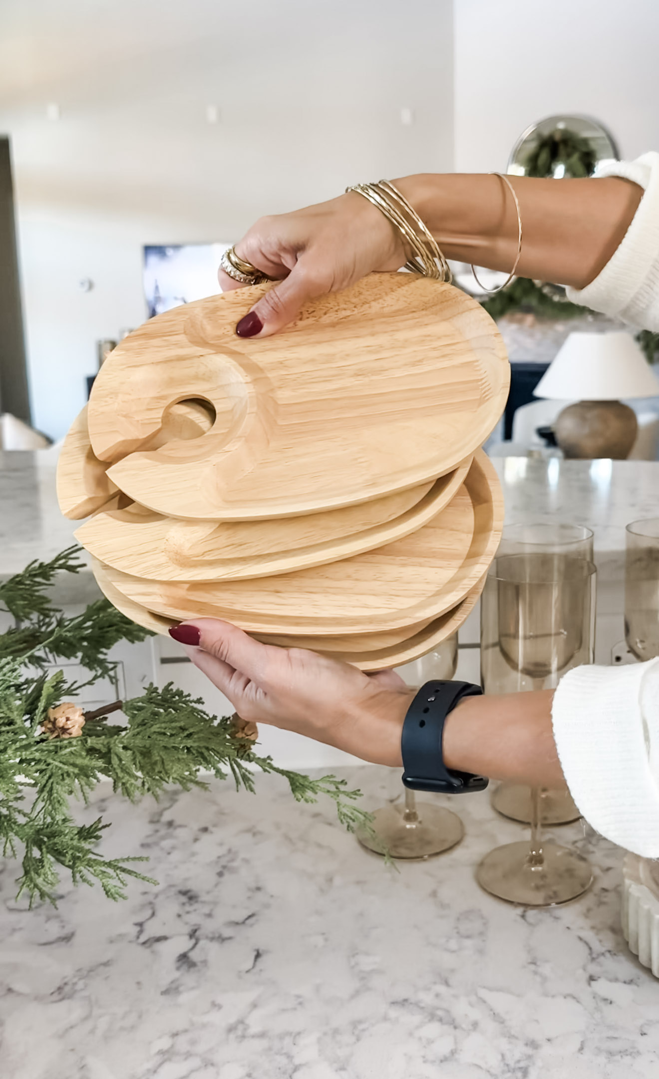 Stack of round wooden serving plates perfect for holiday entertaining, displayed with festive greenery and gold accents in a bright, neutral kitchen.