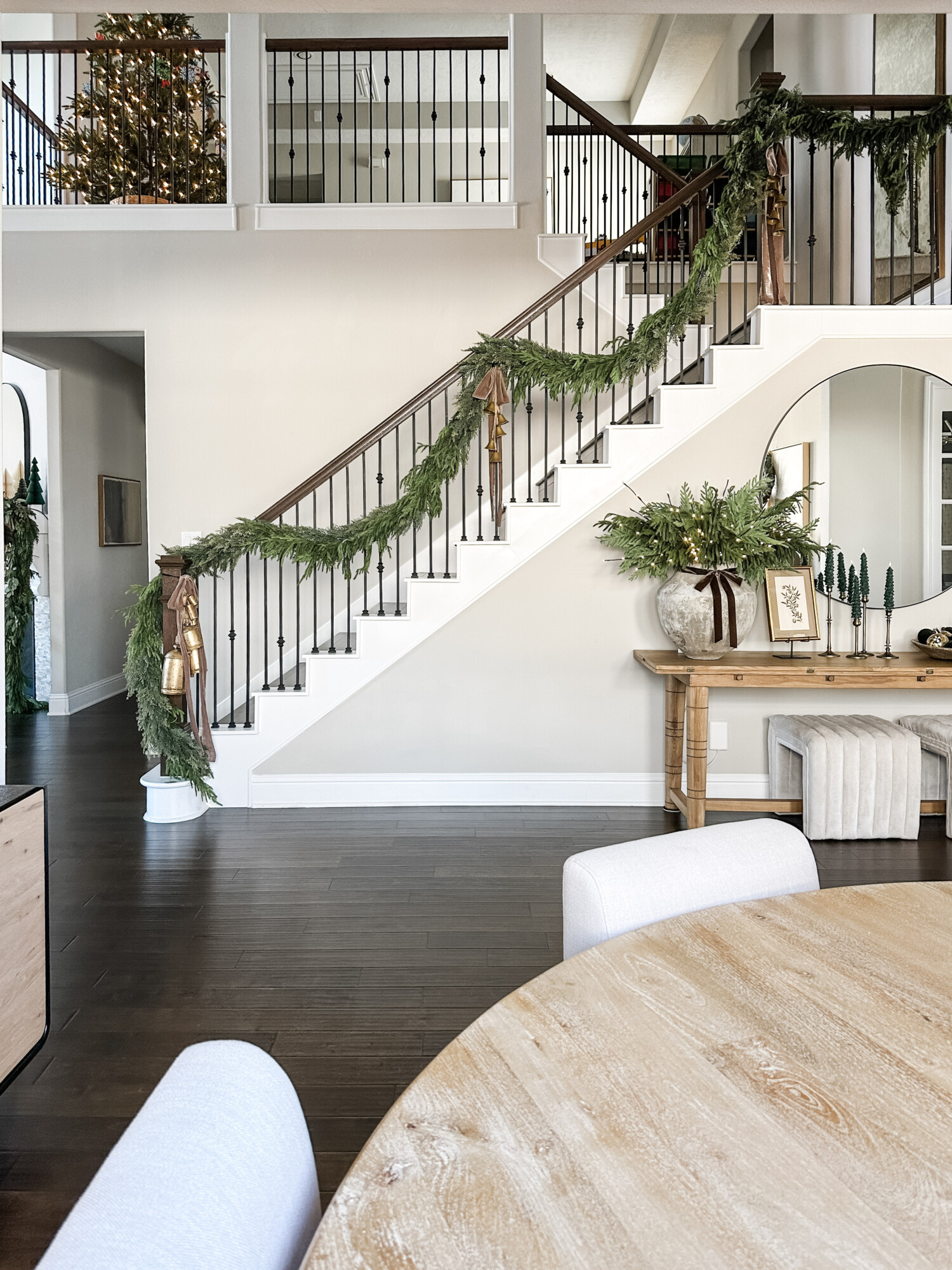 Neutral dining room with large greenery centerpiece, simple holiday wreath, and white dining chairs styled for Christmas