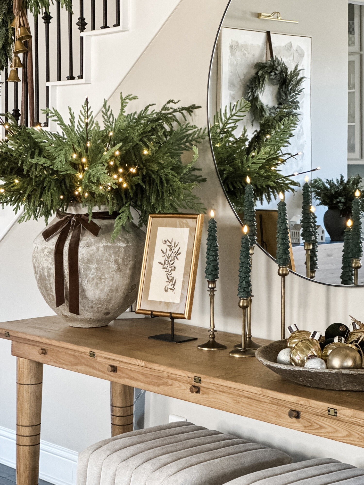 Holiday console table with oversized greenery arrangement, gold framed art, green taper candles, and bowl of ornaments