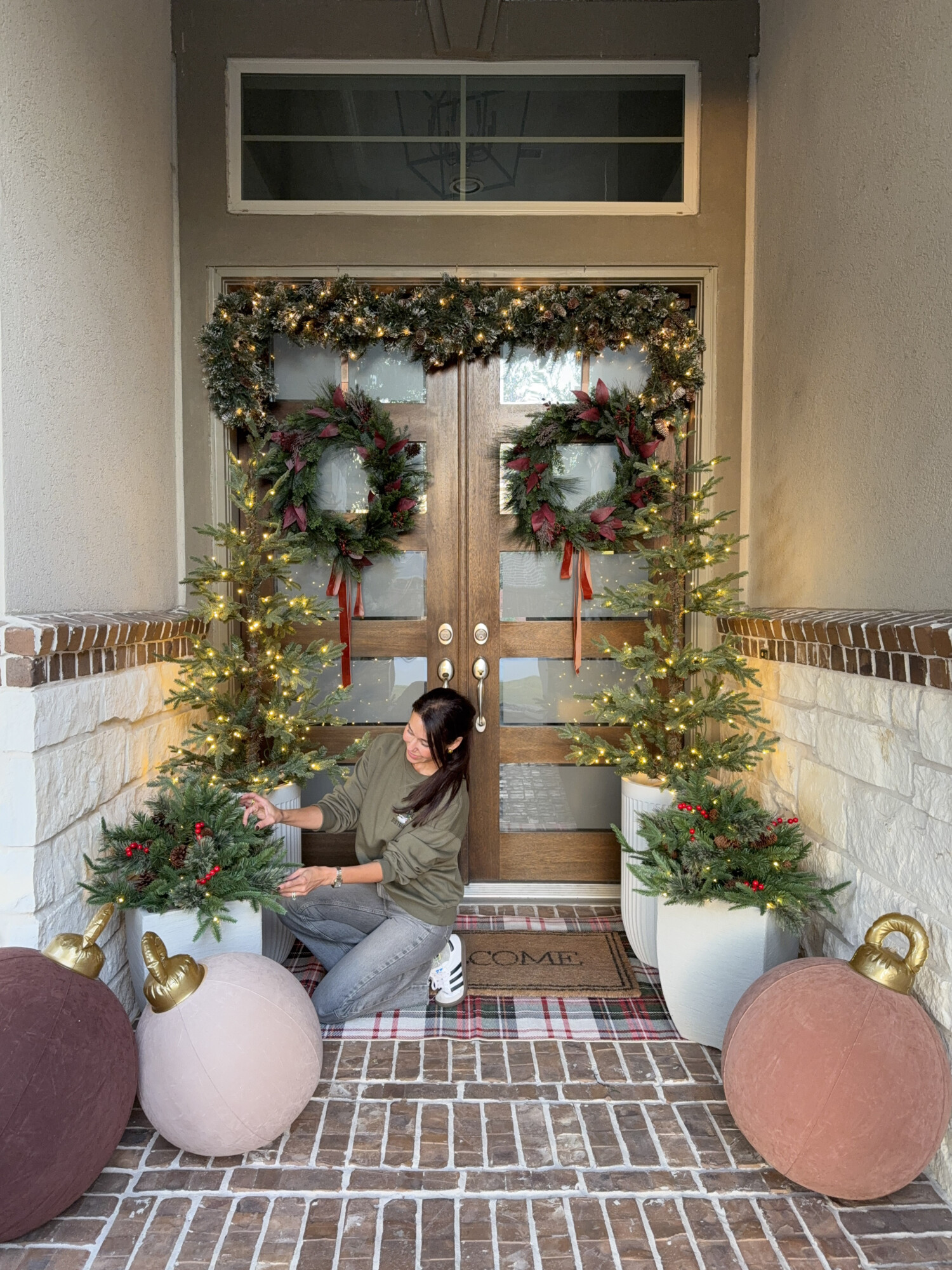 Mariana arranging greenery and lights on a festive front porch Christmas setup.