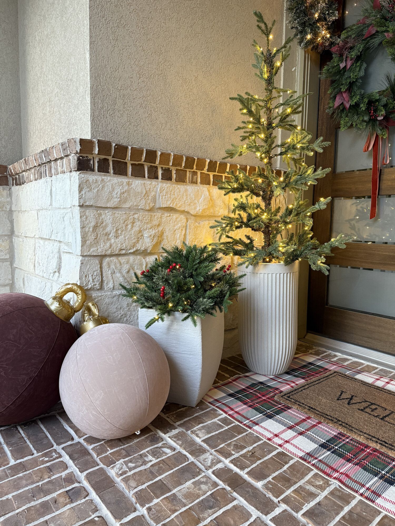 Pre-lit potted Christmas trees and winter greenery in white planters.