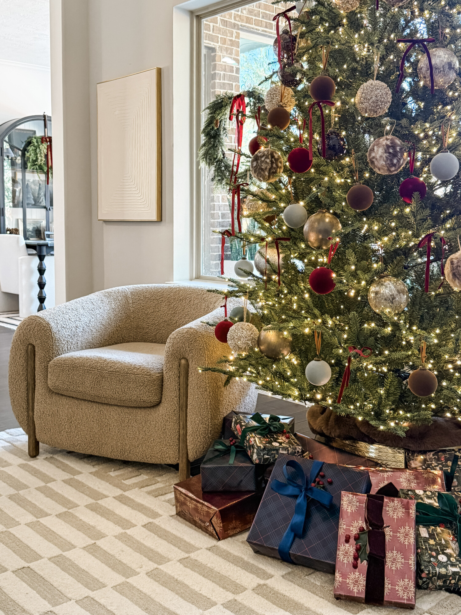 Neutral living room with a decorated Christmas tree, wrapped gifts, and a cozy accent chair styled for the holidays