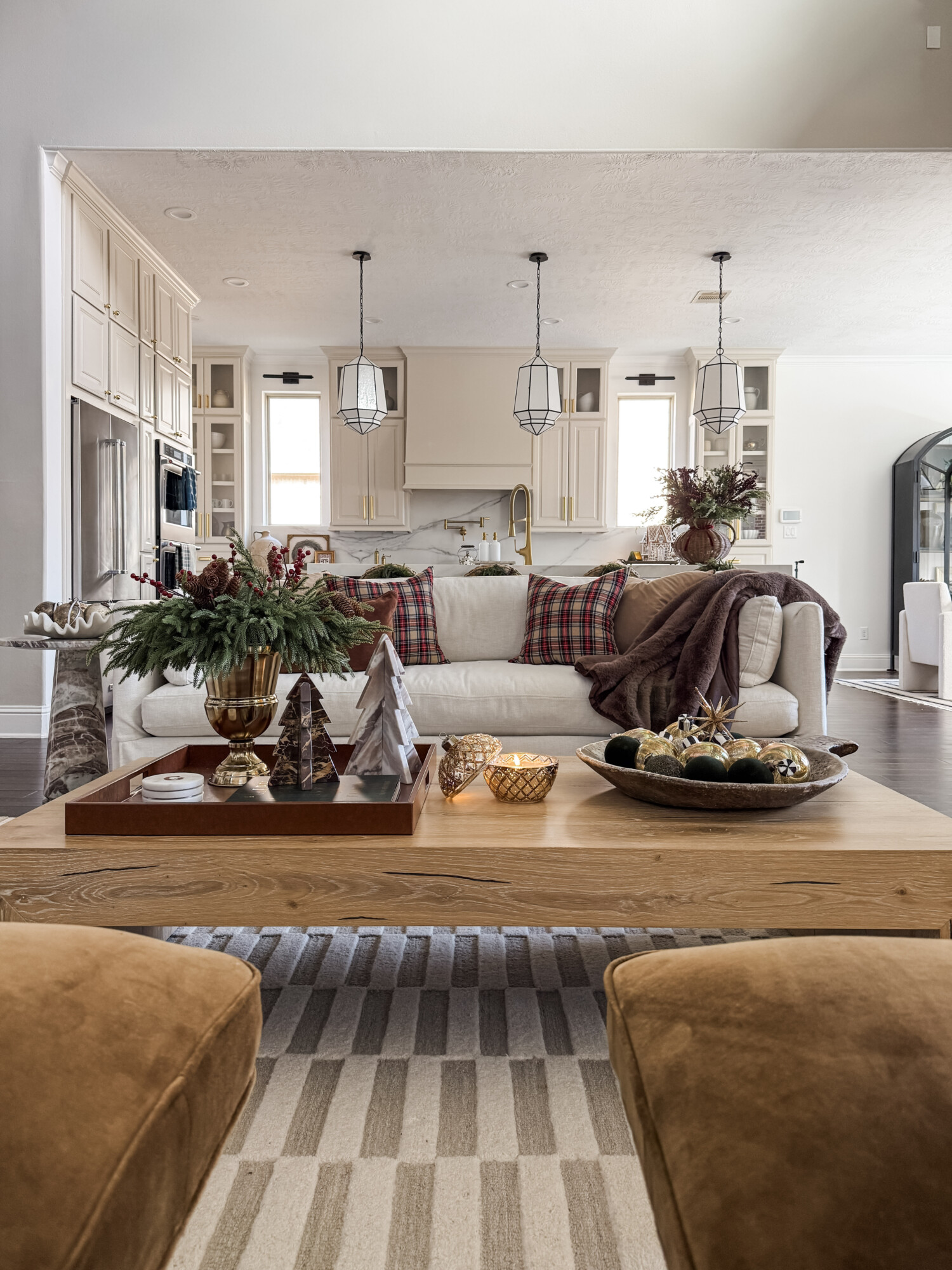 Coffee table styled with greenery in a gold vase, sculptural trees, gold and green ornaments, and warm candlelight for an elevated holiday display.