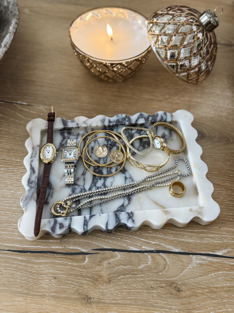 Gold jewelry and watches styled on a marble tray with a decorative candle