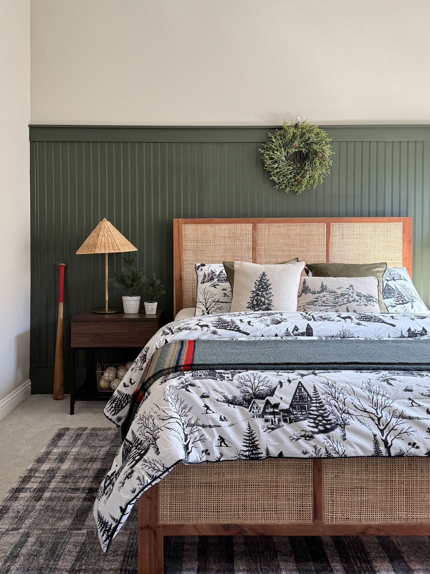 Bedroom with green board and batten accent wall, winter themed bedding, a wreath above the bed, and natural textures creating a calm holiday retreat.