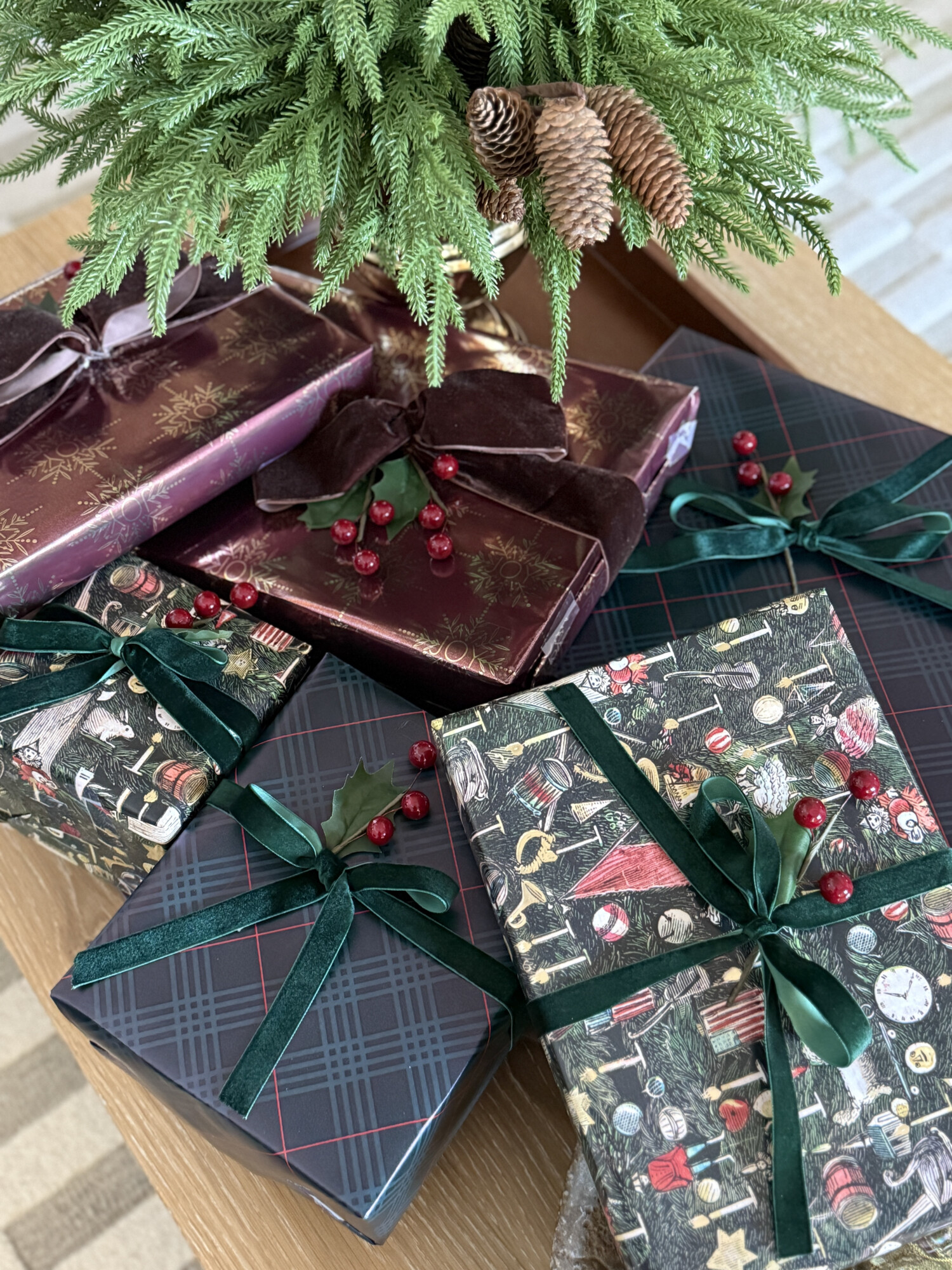 Wrapped Christmas gifts with festive patterned wrapping paper, green velvet ribbon, and pine greenery accents