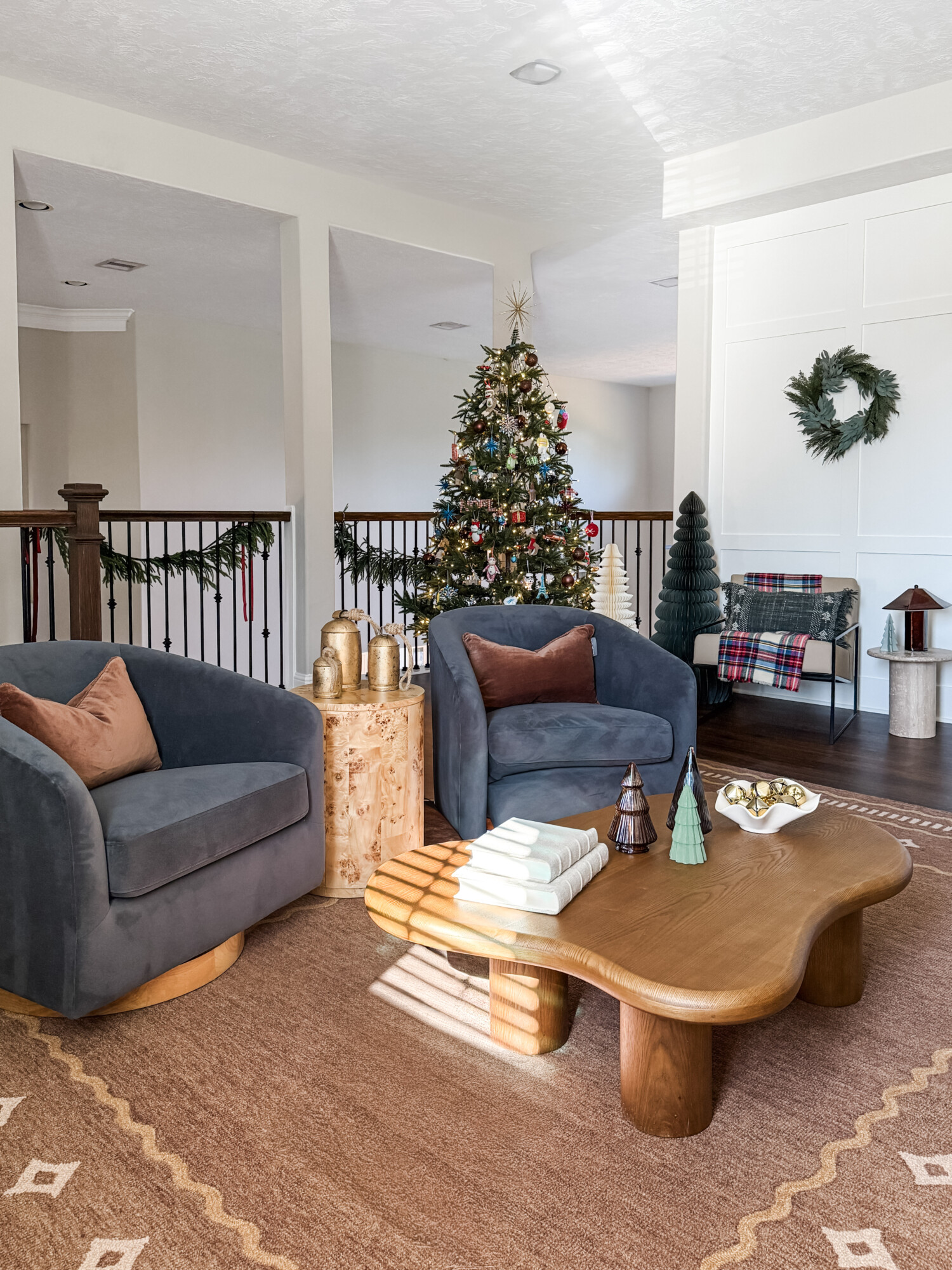 Kids’ playroom decorated with a nostalgic Christmas tree, cozy blue swivel chairs, a sculptural wood coffee table, and playful holiday accents in a warm, inviting space.